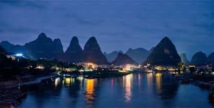 Panorama of Yangshuo town illuminated in the evening with dramatic karst mountain landscape in background over Li river. Yangshuo, China