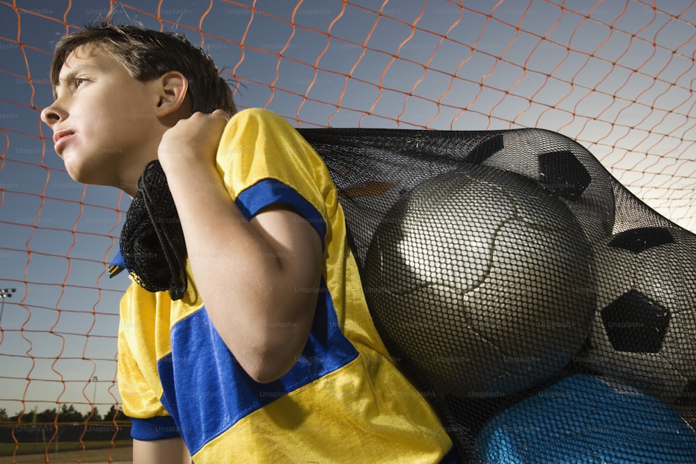 a boy in a yellow and blue shirt leaning against a net
