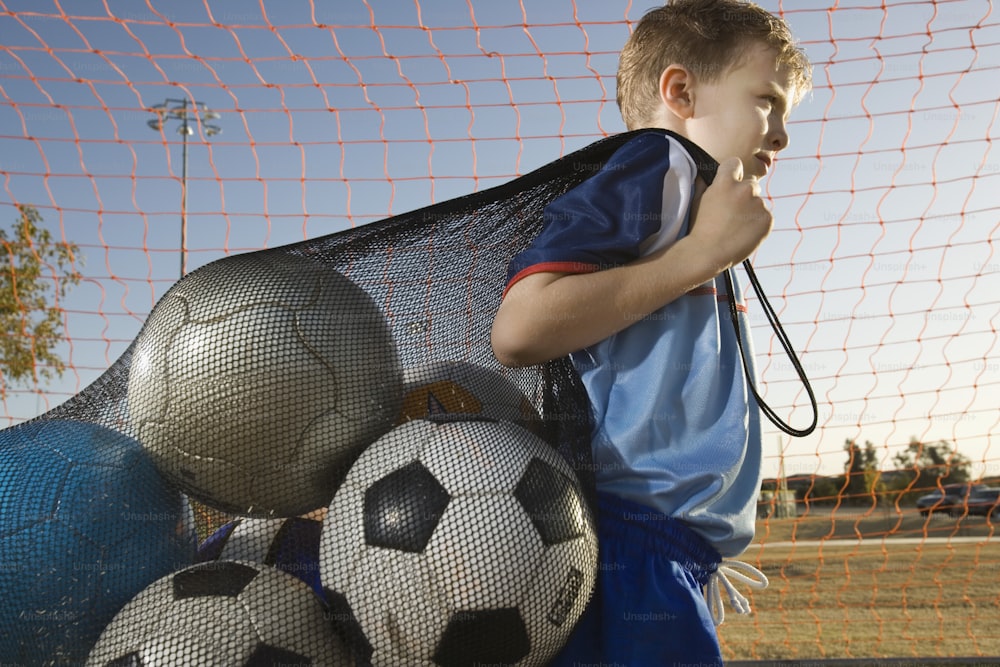 um menino ao lado de uma pilha de bolas de futebol