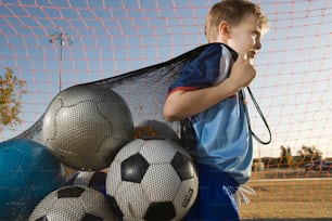 a young boy standing next to a pile of soccer balls