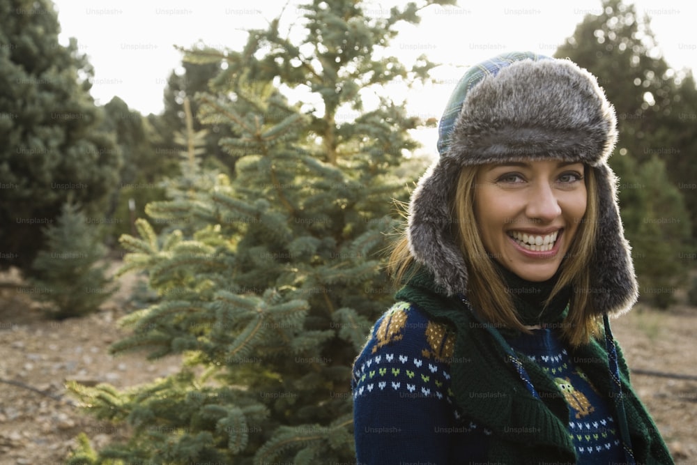 a woman wearing a hat and scarf in front of a christmas tree