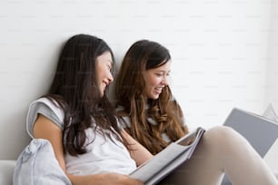 ベッドに座って本を見ている2人の若い女性