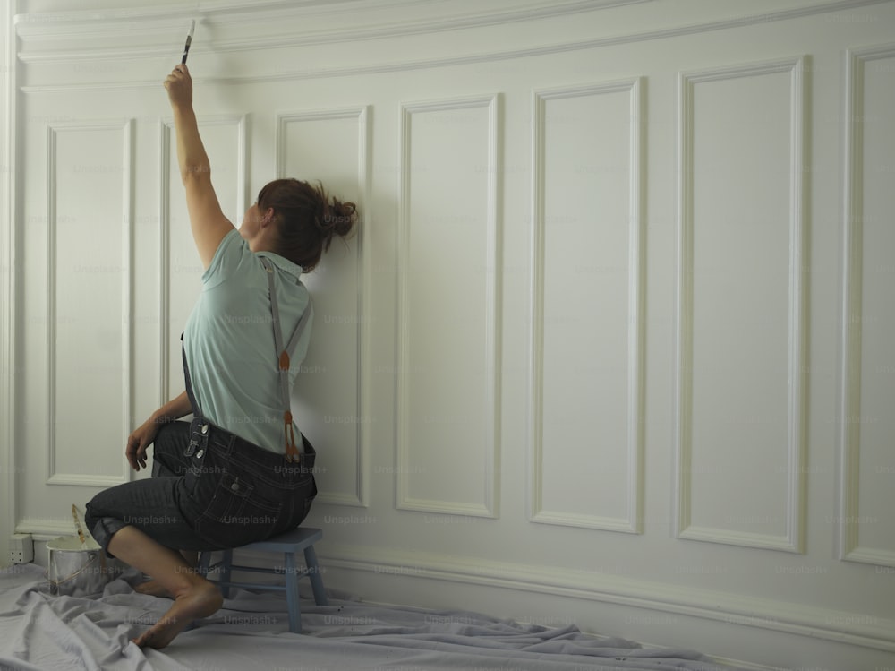 a woman painting a wall with a paint roller