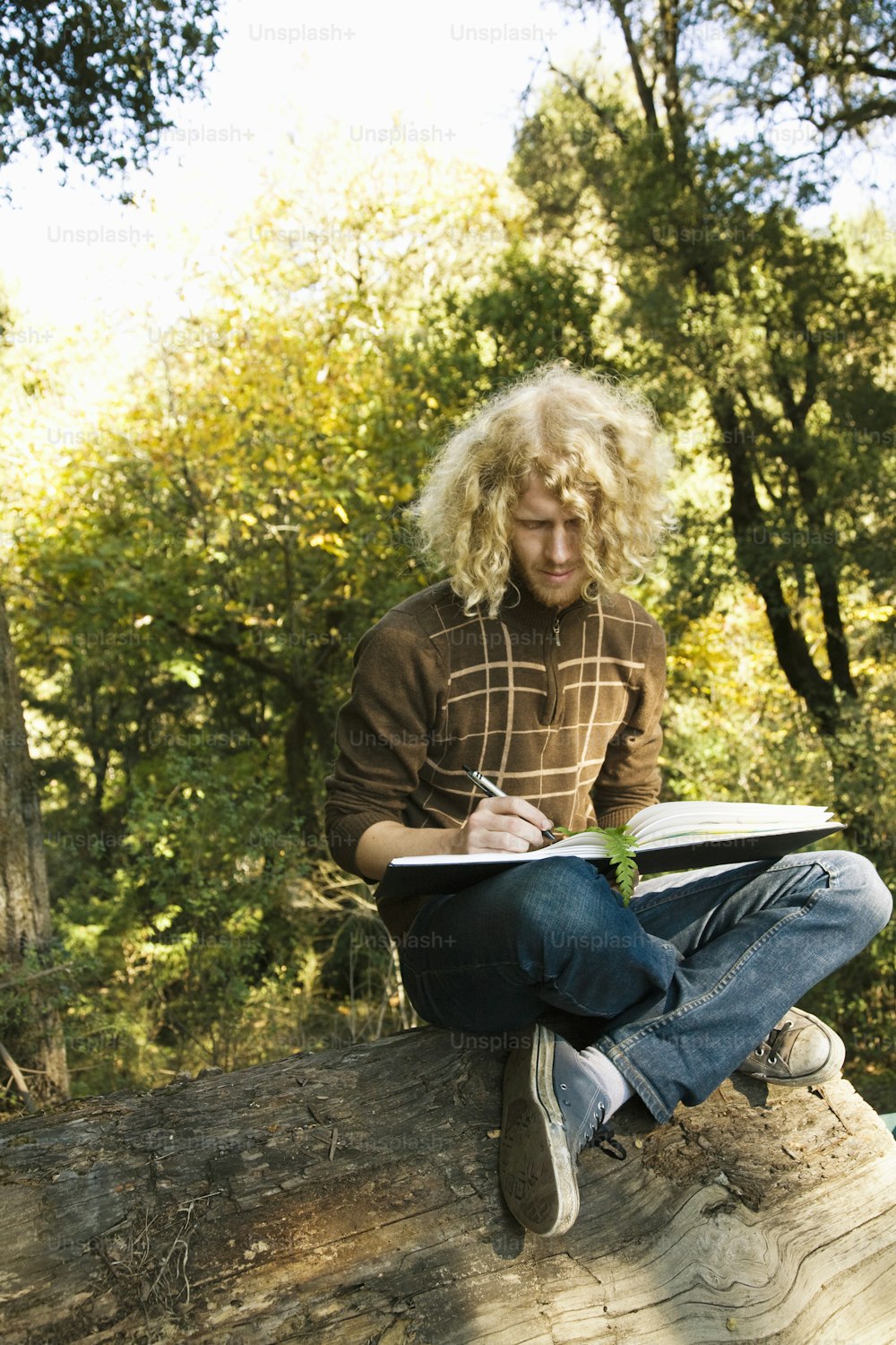 Un hombre sentado en un tronco escribiendo en un trozo de madera