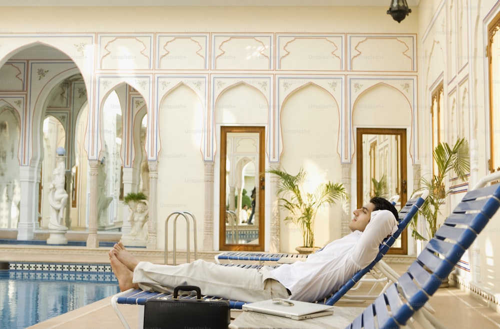 a man laying on a lounge chair next to a swimming pool