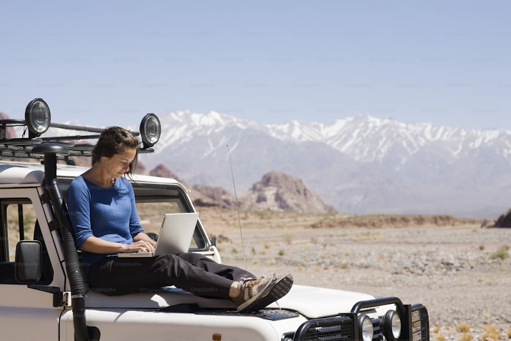 a man sitting on the back of a truck using a laptop computer