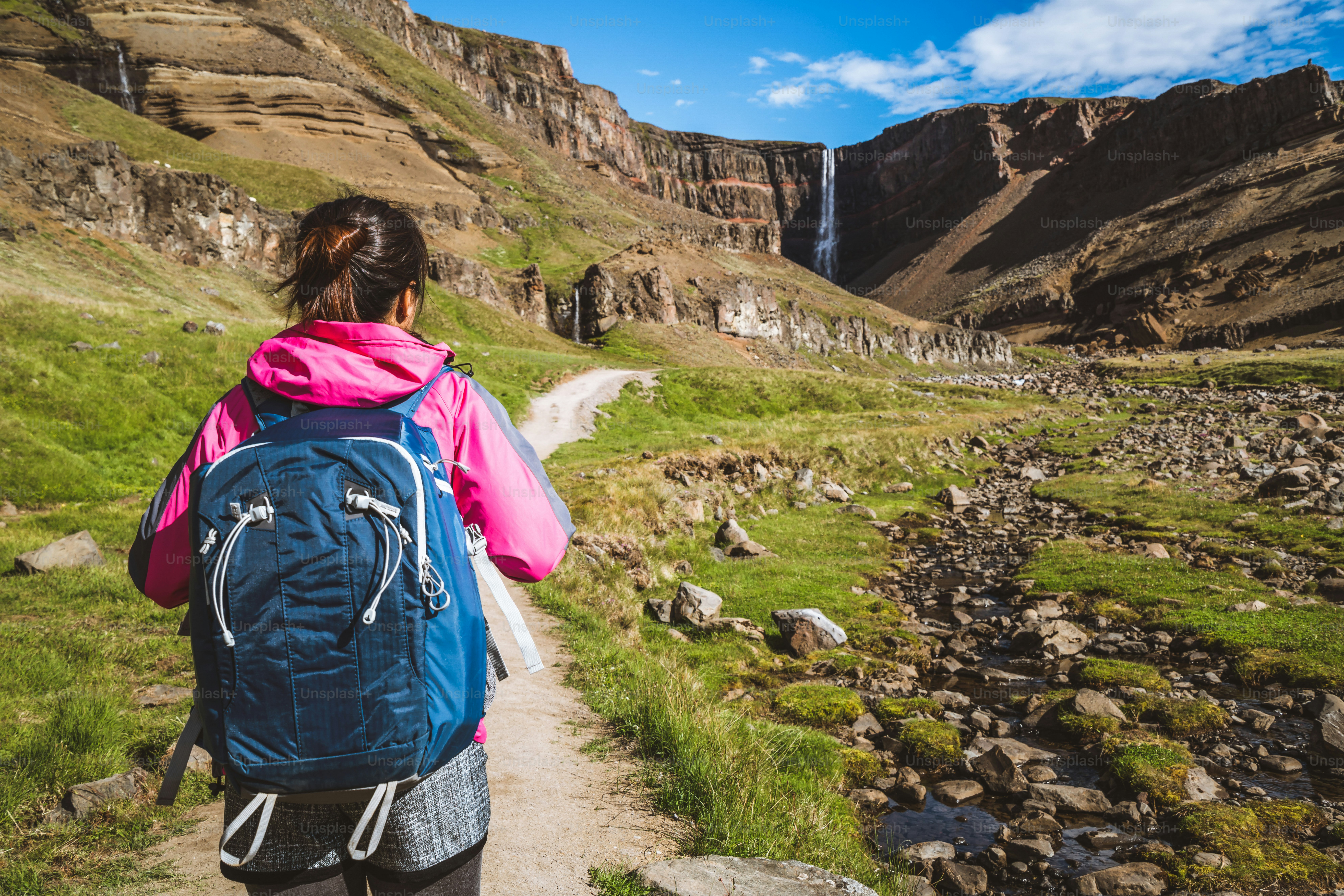 Woman traveler trekking in Icelandic summer landscape at the Hengifoss waterfall in Iceland. The waterfall is situated in the eastern part of Iceland.