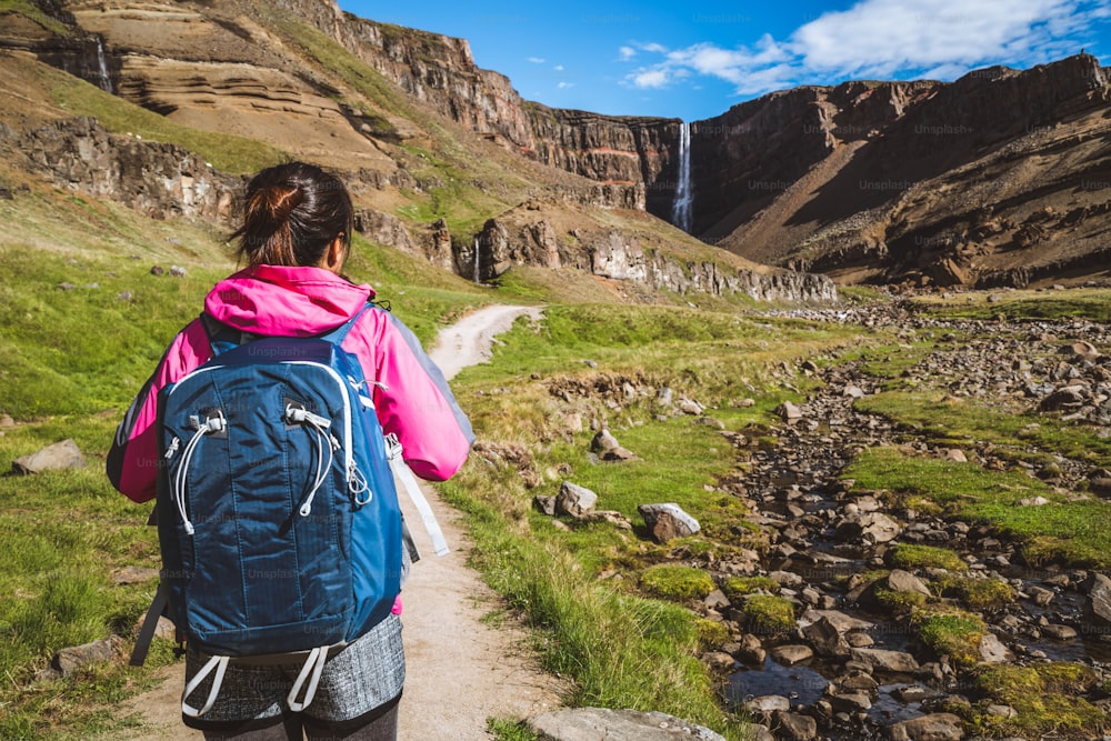 Mujer viajera haciendo senderismo en el paisaje de verano islandés en la cascada de Hengifoss en Islandia. La cascada está situada en la parte oriental de Islandia.