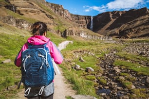 Woman traveler trekking in Icelandic summer landscape at the Hengifoss waterfall in Iceland. The waterfall is situated in the eastern part of Iceland.