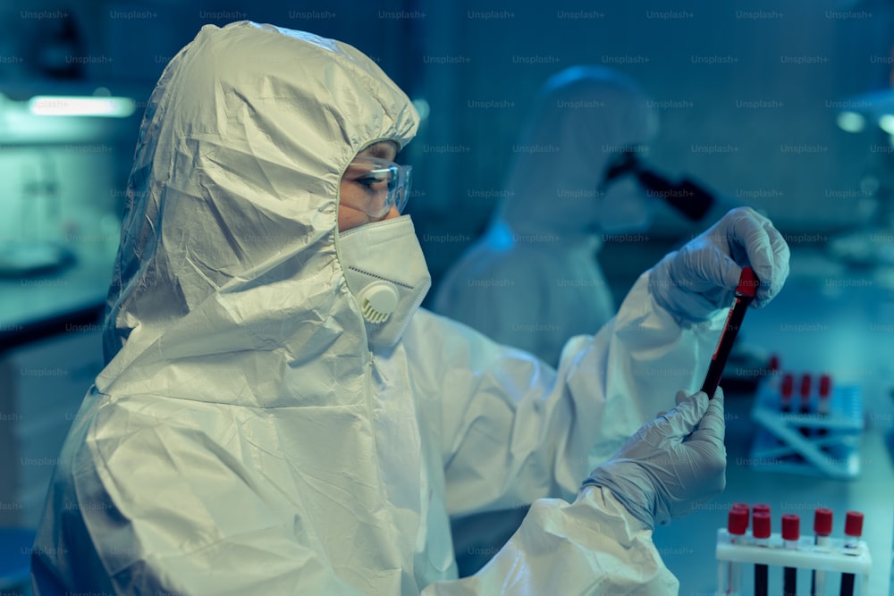 Scientist or chemist in coveralls holding vacutainer with biomaterial