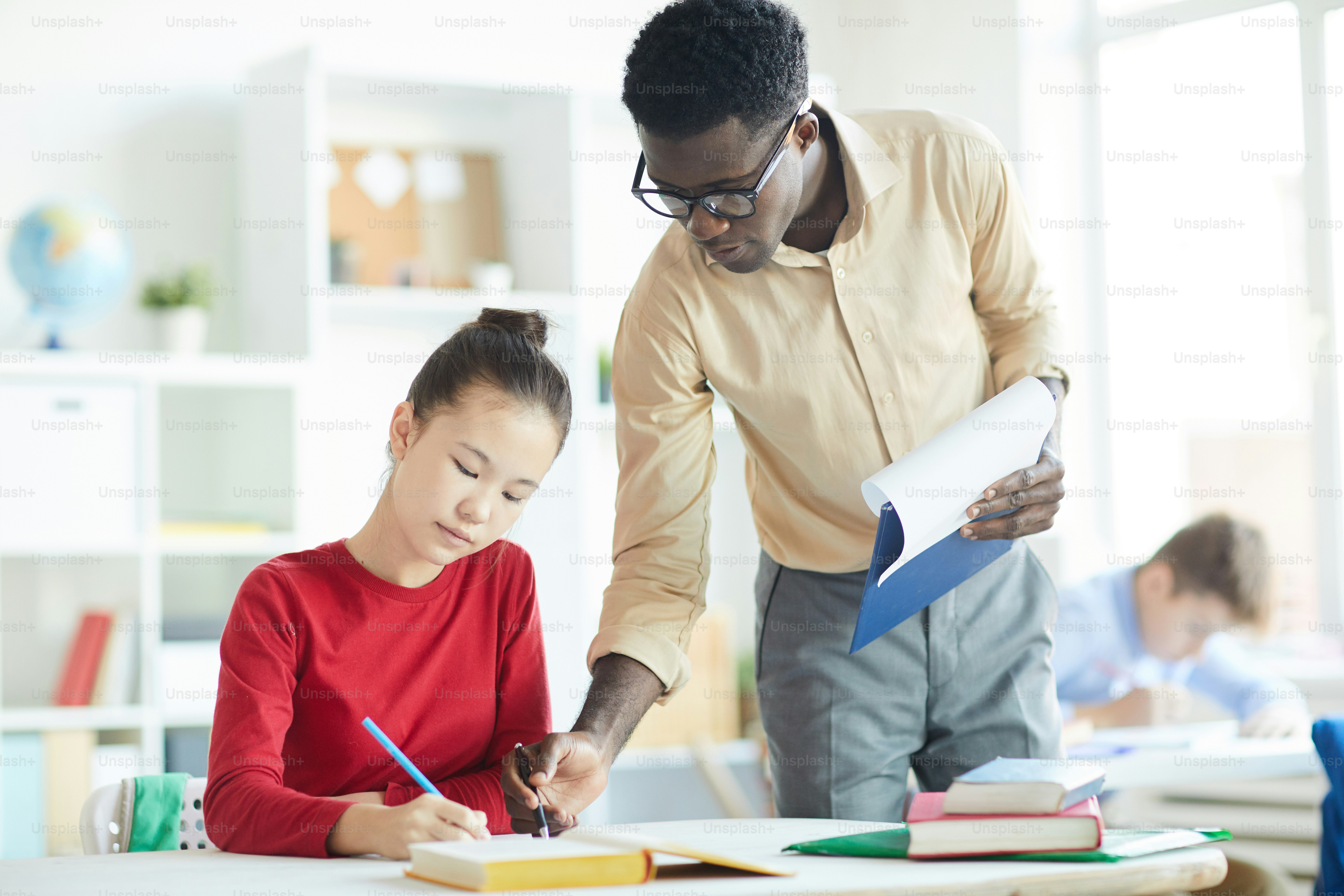 Une enseignante afro-américaine pointant du doigt les notes d’une écolière tout en lui expliquant comment corriger une erreur