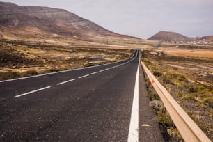 Lange gerade Straße mitten in einer Niemandslandschaft auf Fuerteventura, um die Insel zu überqueren und sich zu bewegen. Alternativer Wind-Lifestyle, der an einem Ort lebt, an dem niemand sonst übernachtet. Abenteuergeist am Reisen