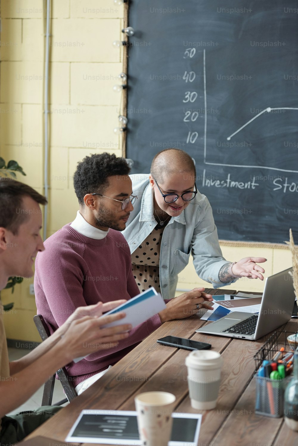 Young female business coach consulting biracial businessman in front of laptop among busy co-workers at seminar or training