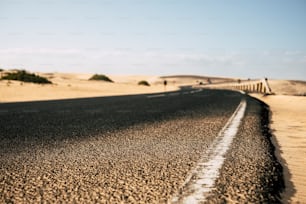 側面に砂漠の砂丘と黒いアスファルトの長い道路の視点の地面のクローズアップポイント - 旅行と目的地の代替夏休みのコンセプトを探る - 最初の部分と焦点ぼけたbackgorundに焦点を当てる