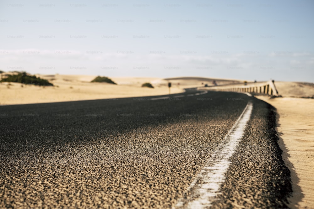 Punto de vista de primer plano del suelo de la carretera larga de asfalto negro con dunas de arena del desierto a los lados: viaje y explore el concepto alternativo de vacaciones de verano del destino: concéntrese en la primera parte y el backgorund desenfocado