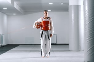 Schöne kaukasische junge Frau mit Pferdeschwanz, die in Taekwondo steht und in die Kamera schaut.