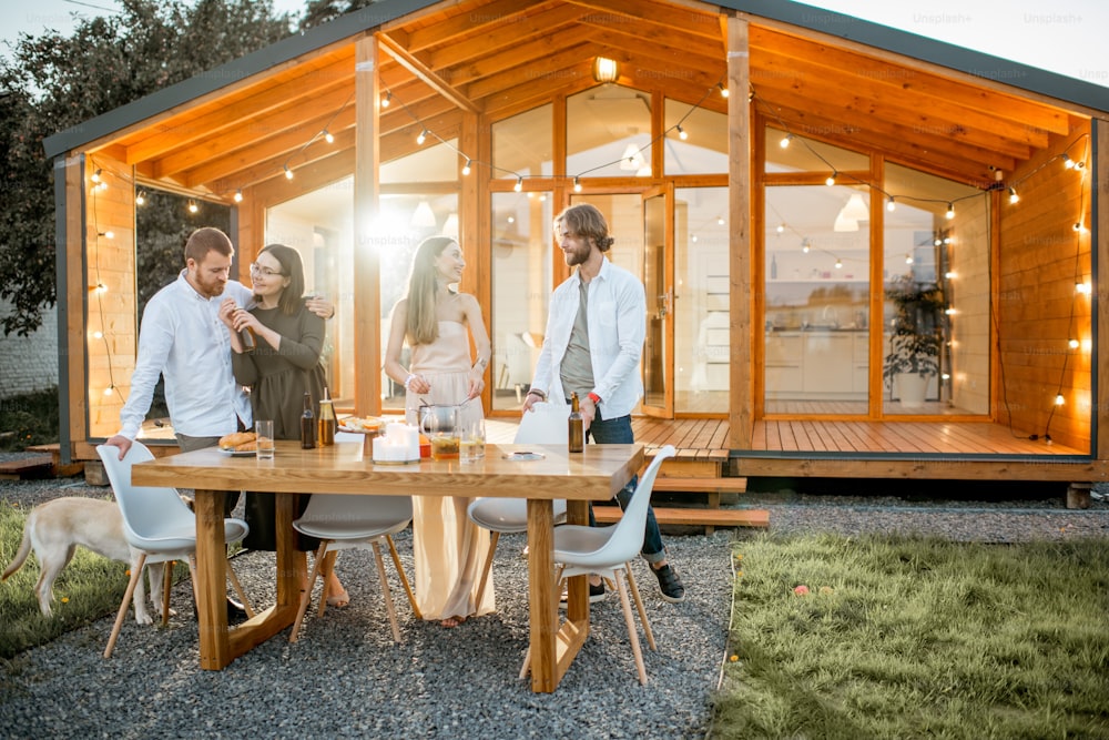 Cuatro amigos disfrutando de la noche cenando en el patio trasero de la moderna casa de campo al aire libre
