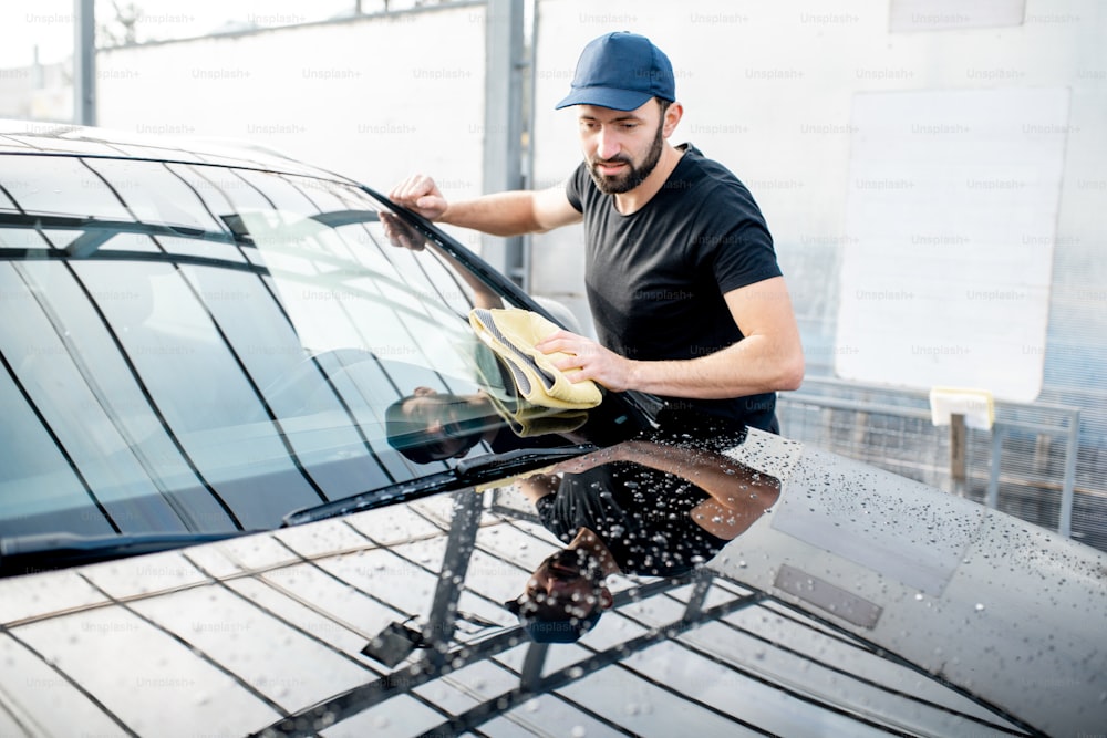 Lavadora profissional em camiseta e touca limpando para-brisa com microfibra amarela na lavagem de carros ao ar livre