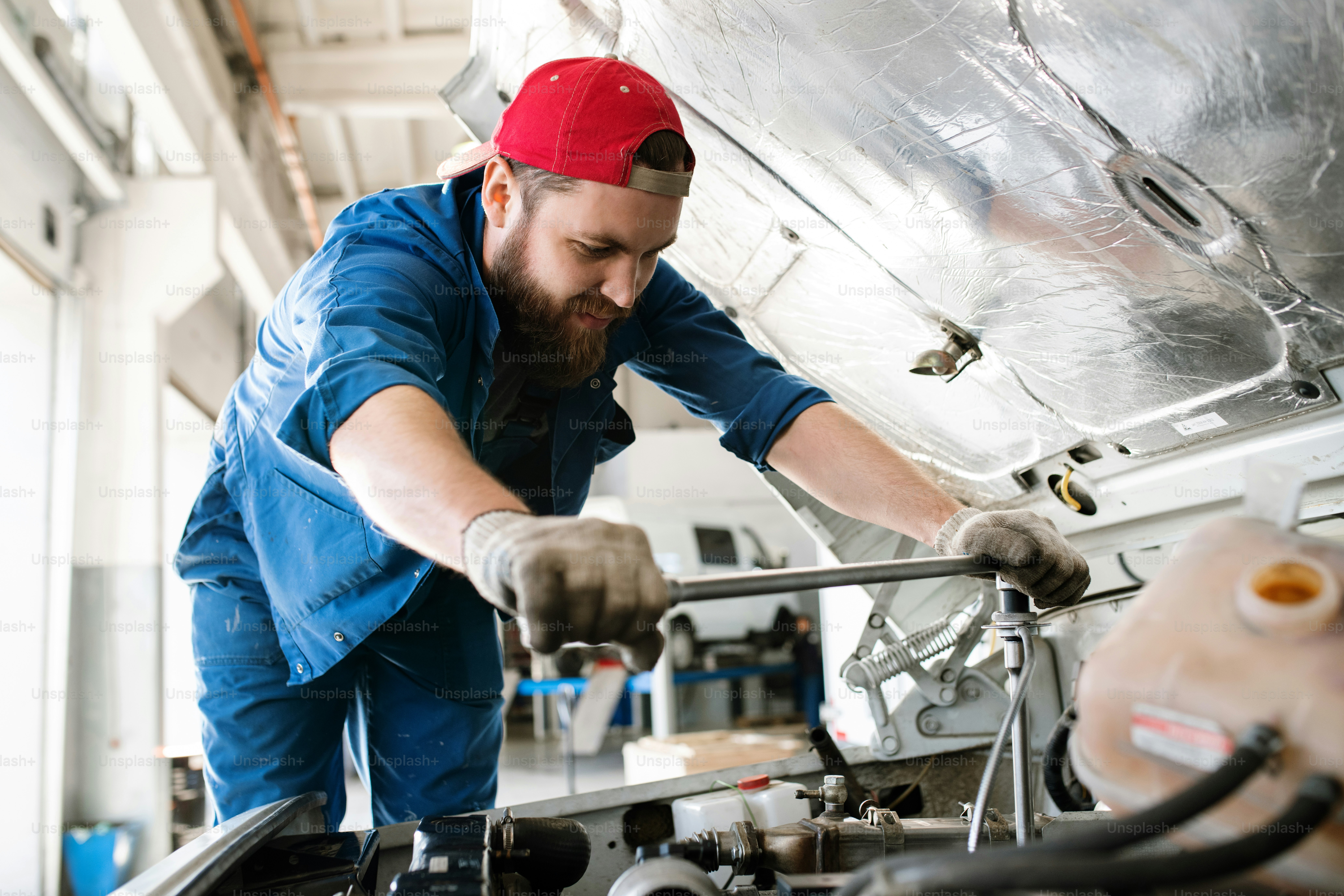 Young technician in workwear bending over engine of car or lorry while checking or fixing small details