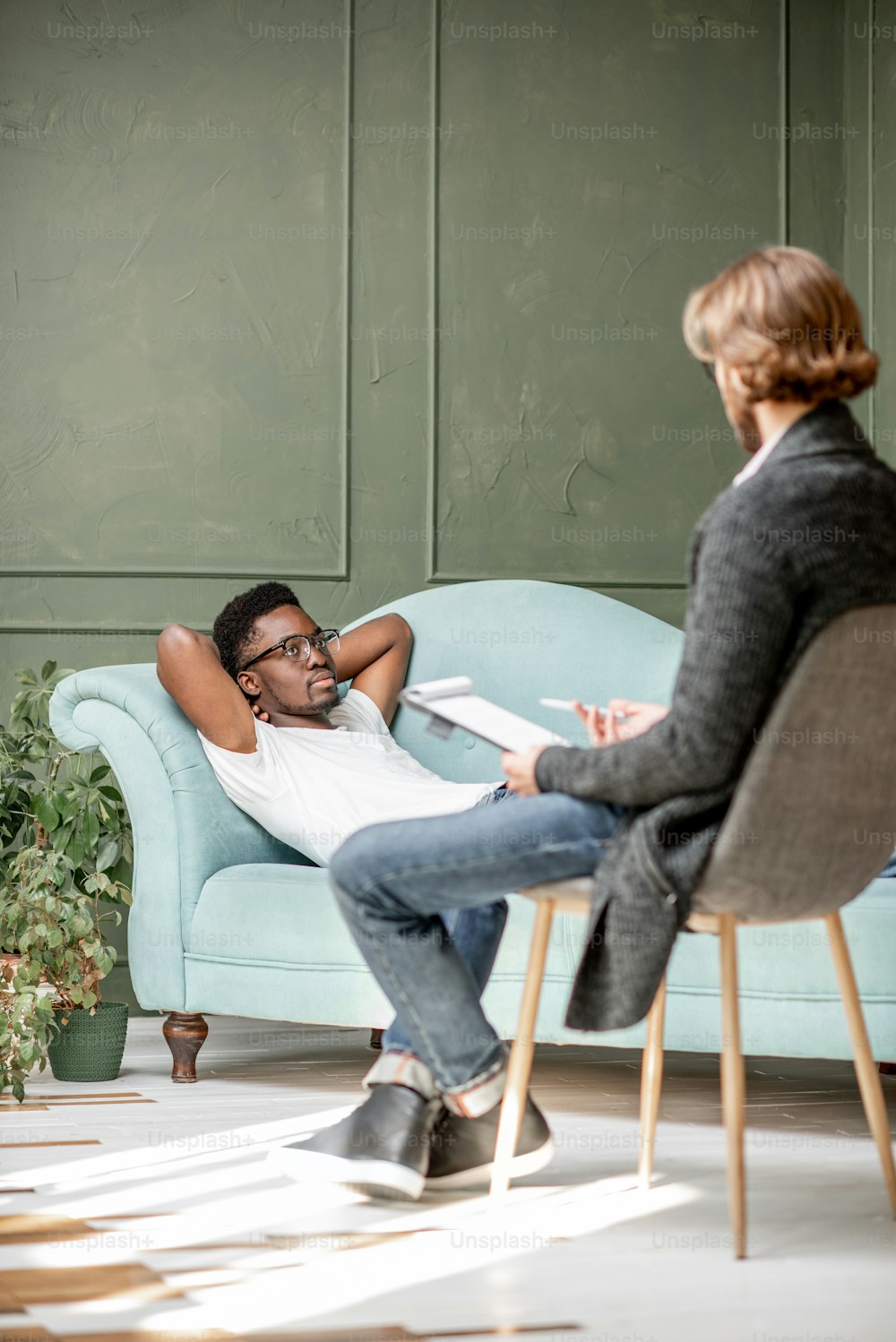 Young afro ethnicity man having a serious conversation with psychologist lying on the comfortable couch during psychological session in the office. Image with copy sopce