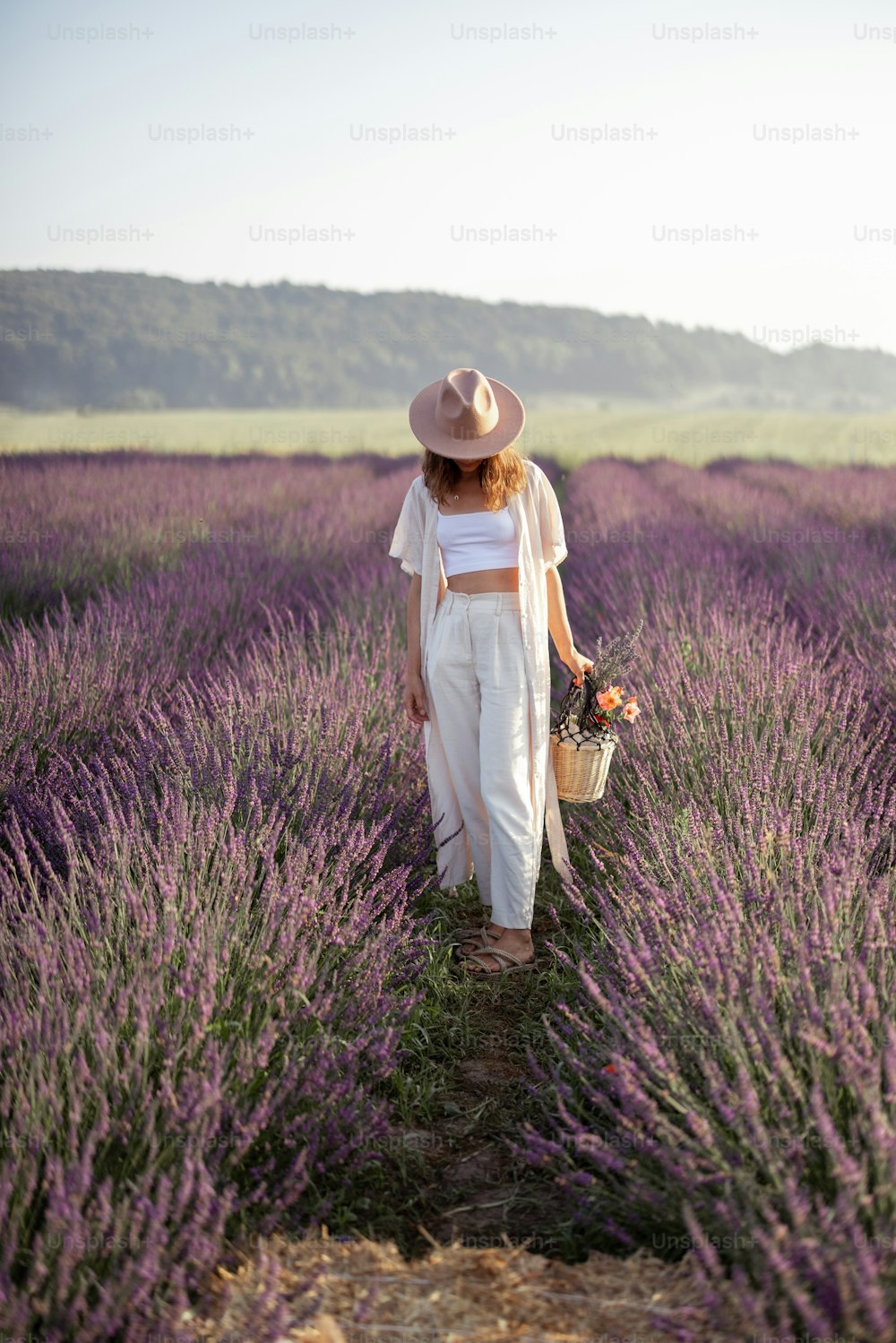 Mujer joven con sombrero que se queda en el campo de lavanda con ramo de flores y disfruta de la belleza de la naturaleza. Calma y concepto consciente. Espacio de copia