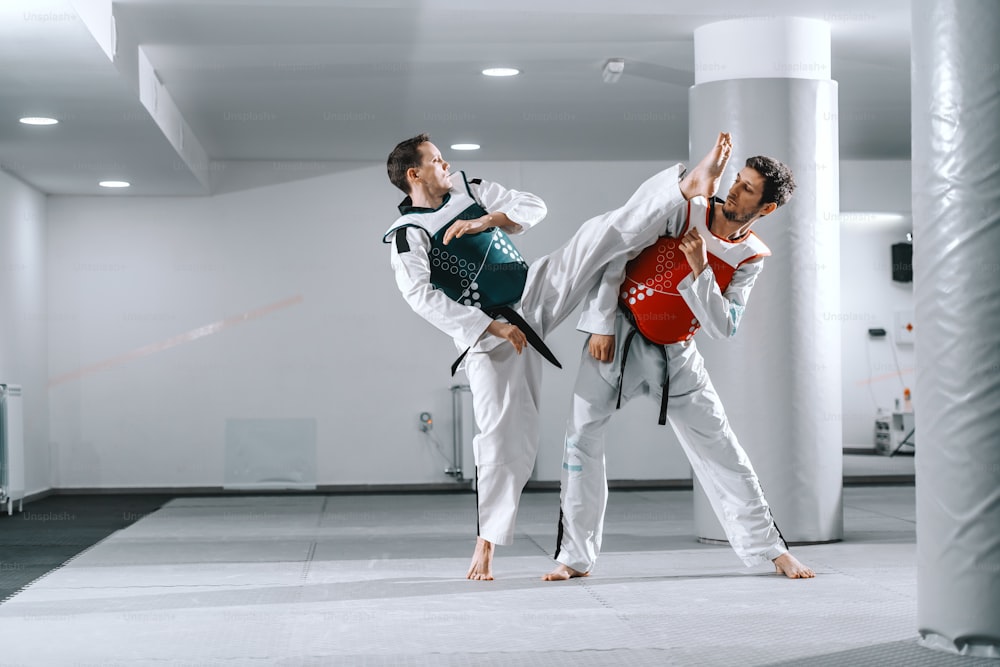 Two Caucasian sporty men sparring in tekwondo fittings barefoot.