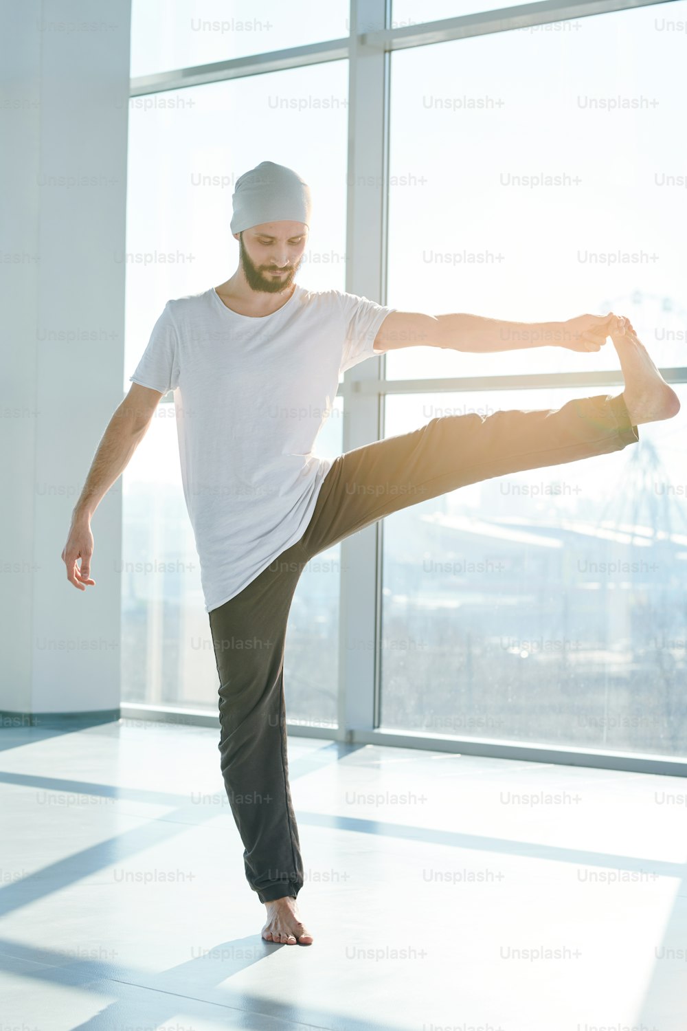 Giovane uomo attivo che allunga la gamba sinistra mentre si trova su quella destra e pratica l'esercizio di yoga