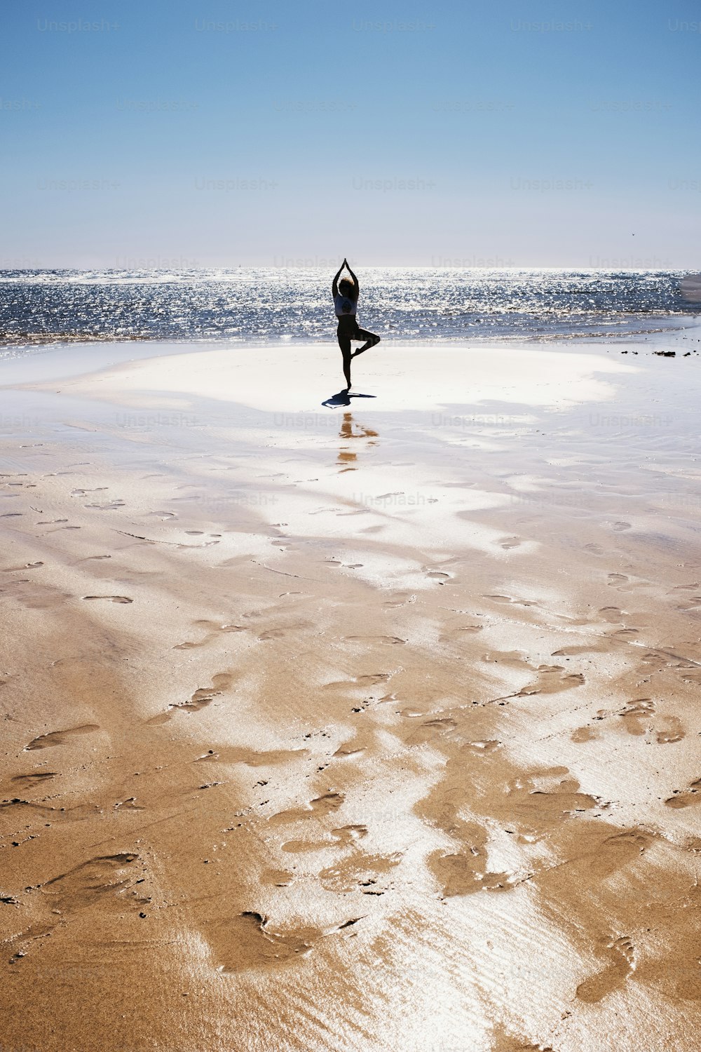 Postura equilibrada de yoga para la mujer en silueta de pie en la playa con el mar del océano azul y el agua en el fondo. Concepto de estilo de vida saludable y personas de vacaciones de verano