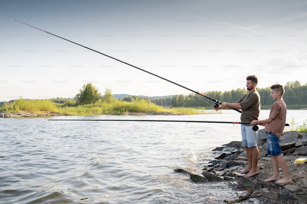 Ragazzo adolescente e suo padre che pescano insieme in riva al lago nel fine settimana estivo