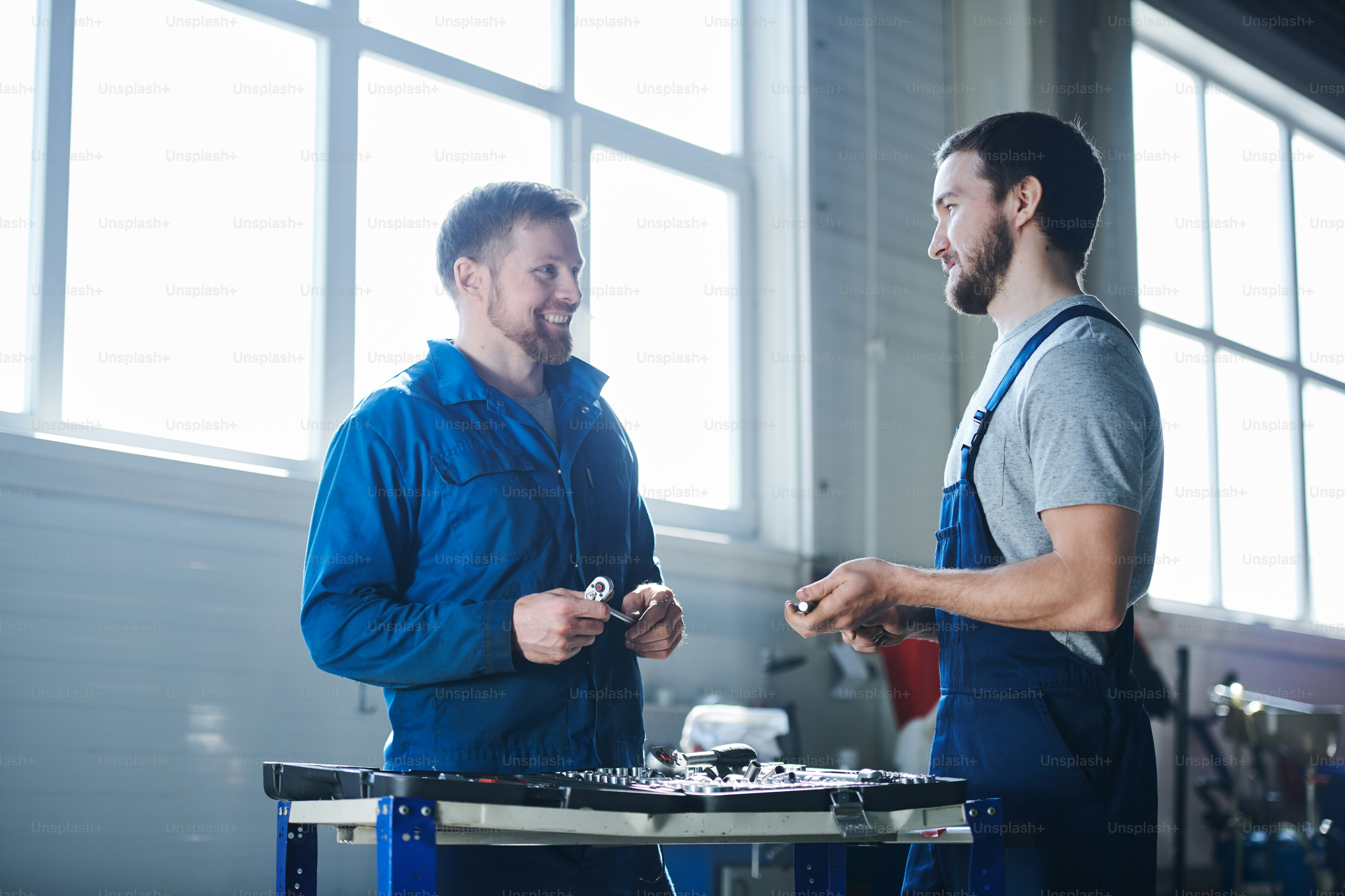 Dois jovens especialistas bem-sucedidos em vestuário de trabalho olhando um para o outro durante a discussão de momentos de trabalho no hangar