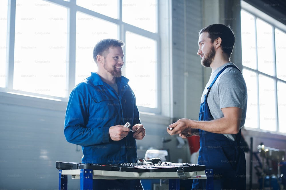 Two young successful specialists in workwear looking at one another during discussion of working moments in hangar