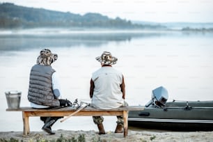 Nonno con figlio seduto insieme sulla panchina mentre pesca sul lago la mattina presto, vista posteriore
