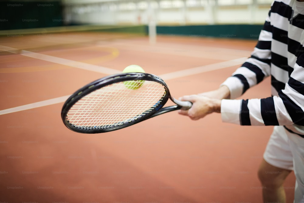 Jugador de tenis activo golpeando la pelota de tenis con la raqueta durante el juego exitoso en el estadio
