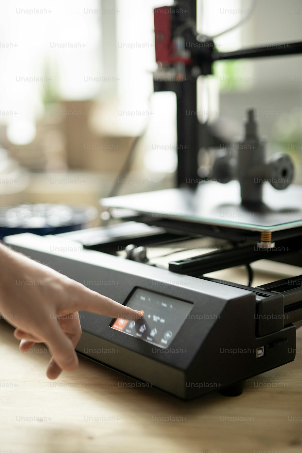 Mano de un joven diseñador que presiona el botón de inicio en el panel de control de la impresora 3D antes de comenzar el proceso de trabajo