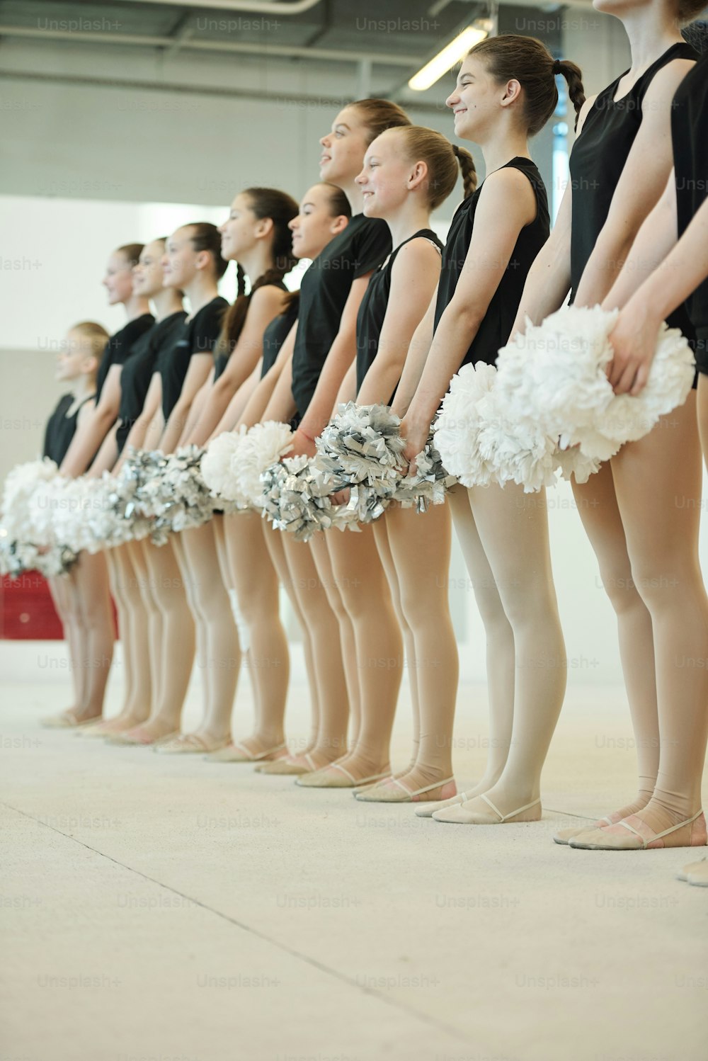 Cheerful teenage participants of cheerleading competition holding pompoms and standing in line