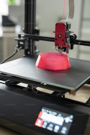Printhead of 3d printer over part of pink round object on working surface during process of printing