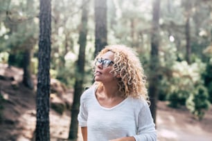 Beauiful blonde curly woman enjoy the outdoor leisure activity in the forest - People in the wood trees nature with defocused background and   sun in backlight
