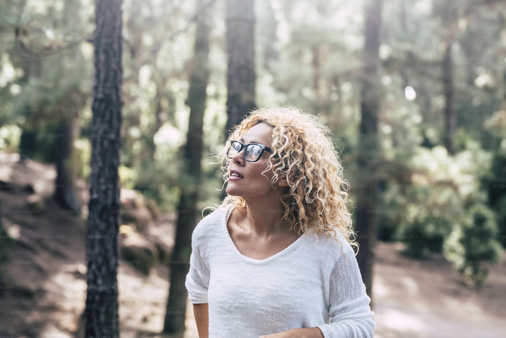 Beauiful blonde curly woman enjoy the outdoor leisure activity in the forest - People in the wood trees nature with defocused background and   sun in backlight