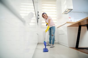 A smiling housewife mopping kitchen floor at home.