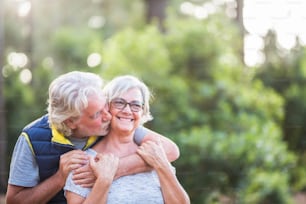 couple of two old people together hugged at the wood or forest - love concept and defocused background - married seniors enjoying the outdoors with kiss and relationship