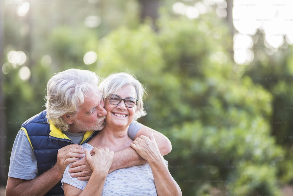 Paar von zwei alten Leuten zusammen umarmt im Wald oder Wald - Liebeskonzept und defokussierter Hintergrund - verheiratete Senioren, die die Natur mit Kuss und Beziehung genießen