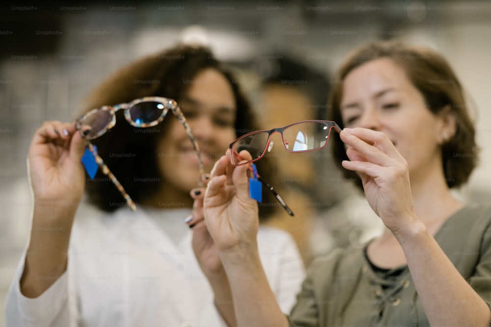 Mãos de jovem consultora e sua cliente comparando dois modelos de óculos de nova coleção enquanto discutiam suas características