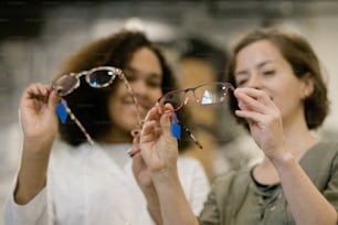 Hands of young consultant and her client comparing two models of eyeglasses from new collection while discussing their characteristics