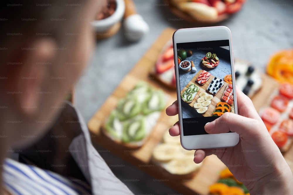 Close up view of female taking photo of healthy freshly made sandwiches with smart phone, top view