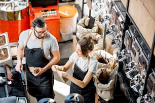 Dos vendedores uniformados llenando y pesando bolsas con café en la cafetería. Vista desde arriba
