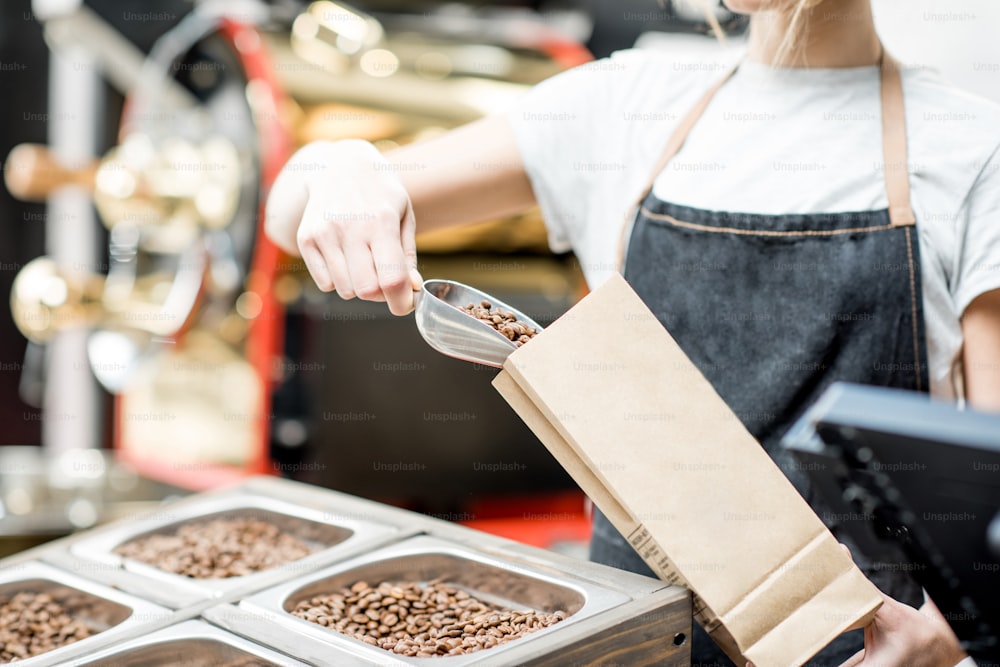 Woman filling paper bag with coffee beans for selling in the store. Close-up view