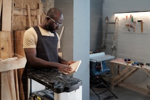 Waist up portrait of African-American man cutting wood in carpentry workshop using electric tools, copy space