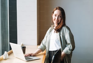 Donna d'affari bruna sorridente adulta quarant'anni con i capelli lunghi in camicia elegante che lavora sul computer portatile nel caffè