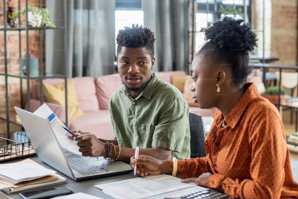 Junges afroamerikanisches Paar sitzt zu Hause am Tisch und analysiert Papiere, während es Steuererklärungen ausfüllt