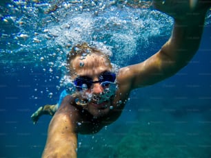 Underwater view of a young diver man swimming and enjoying at the sea for summer vacation while taking a selfie.
